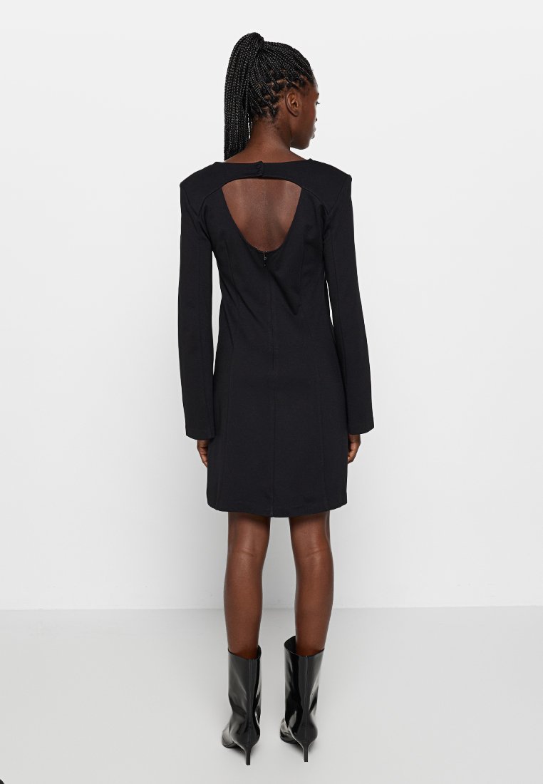 Czarna sukienka z długim rękawem, z dekoltem na plecach, dopasowana sylwetka i zamek błyskawiczny. Gładka tekstura i długość do kolan. Noszone modowe botki.
