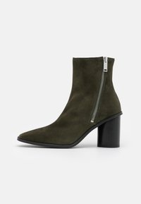 Zielono-oliwkowe zamszowe botki do kostki z ostrym noskiem, bocznym zamkiem błyskawicznym i masywnym czarnym obcasem. Gładka tekstura i elegancki design.