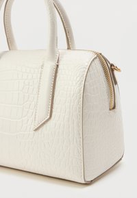 Bela torbica iz teksture krokodila z urejeno obliko, dvojnimi ročaji in zlatim zadrgo, ki prikazuje gladko, sijočo površino.