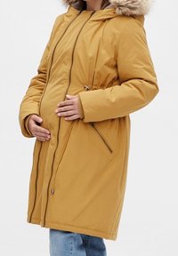 Žlutá těhotenská parka s umělou kožešinou na kapuci, plným zipem, dvěma bočními kapsami a nastavitelnou šňůrkou v pase.