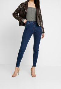 Brun läderjacka över en grå ribbad linne, parat med höga blå skinny jeans och nakna högklackade sandaler.