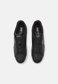 Para czarnych sneakersów Puma ze sznurowadłami, białym logo Puma po bokach oraz tekstem "Forever Better" wewnątrz butów, pokazane z góry.