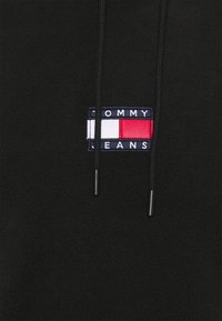 Sort hætte sweatshirt med et lille broderet "Tommy Jeans" mærke i røde, hvide og marineblå nuancer samt sorte snore. Blødt, struktureret materiale.