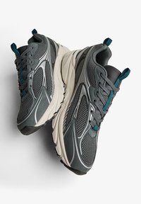 Grå sportskor med en ovandel i mesh och teal detaljer. Har en tjock vit mellansula, gummiyttersula och snörningsdesign.