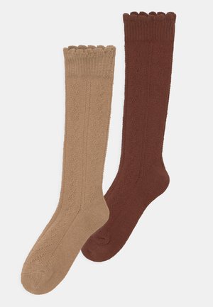 Zwei Paar kniehohe Socken: Eine in Beige mit einem strukturierten Muster und gewelltem Rand, die andere in Dunkelbraun mit glatter Oberfläche.