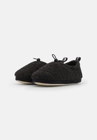 Black indoor slippers made of textured, fluffy material with a round toe shape. Features a contrasting flat sole and two decorative ties.
