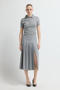 Grijs poloshirt met korte mouwen en knopen, gecombineerd met een geplooide grijze maxirok met een zijsplit, afgemaakt met zwarte hakken.