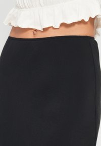 Jupe noire avec une texture lisse et une coupe ajustée. La ceinture est élastique, offrant du confort sans fermeture supplémentaire.