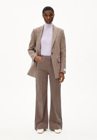 Bruine textuur blazer over een lichtpaarse coltrui en bruine flared corduroy broek, gecombineerd met witte hakken.