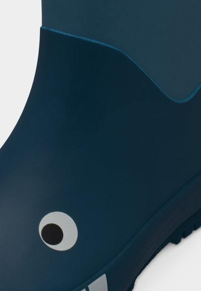 Λαστιχένια βροχερή μπότα σε σκούρο μπλε με στρογγυλεμένη κορυφή, λείο υφή, λευκό μοτίβο ματιού και μαύρες λεπτομέρειες κοντά στη σόλα.