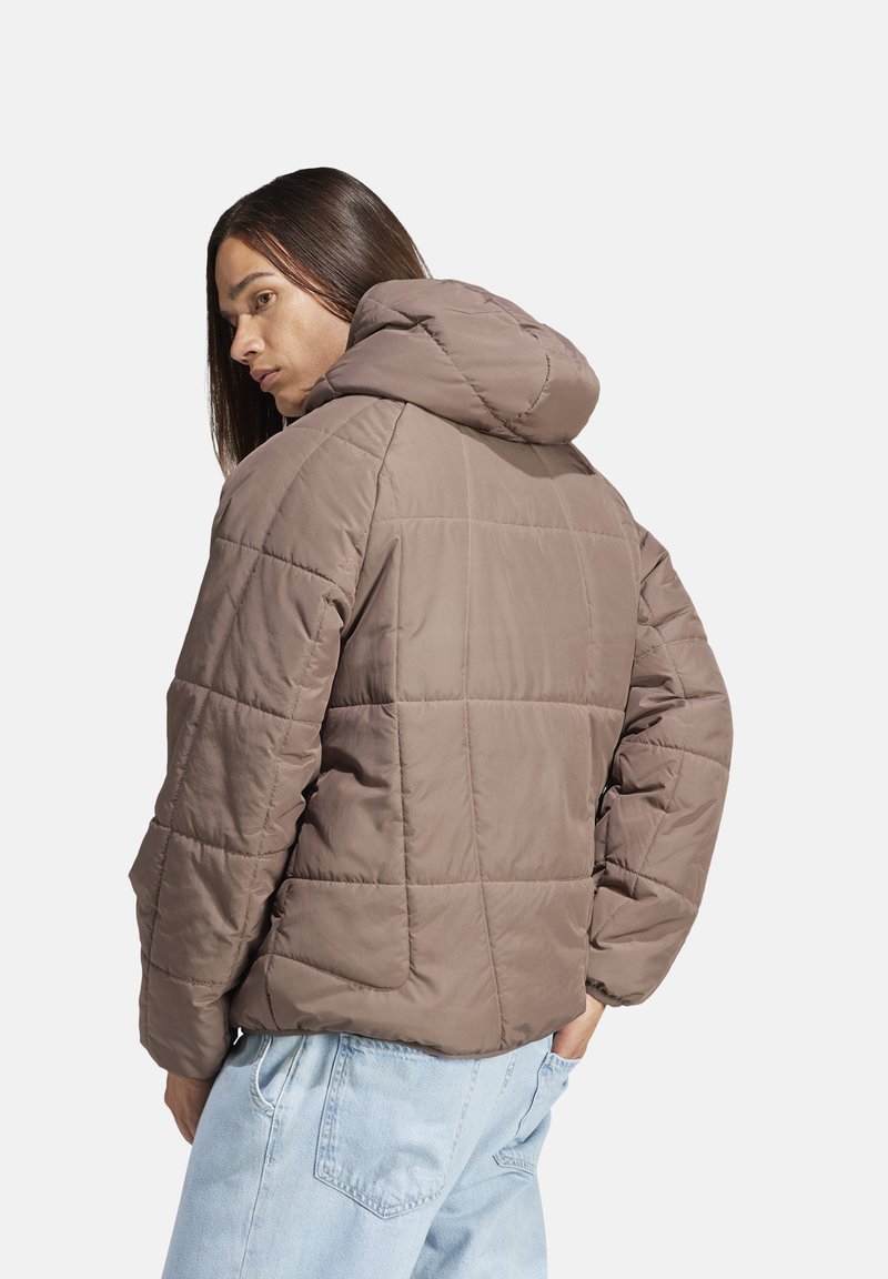Bruine gewatteerde pufferjack met capuchon, met een zachte textuur en een boxy pasvorm, gezien van achteren tegen een plain witte achtergrond.