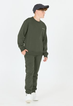 Donkergroene sweatshirt en bijpassende joggers van zacht materiaal. Witte sneakers en een donkere pet maken de outfit compleet. Minimalistisch ontwerp met logodetail.