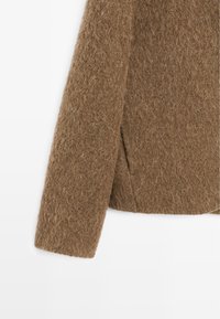 Brown fuzzy wool sweater sleeve with side slit detail on white background.