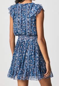 Sinivihreä kukkamekko, jossa on riepuhihaiset hihat, istuva vyötärö ja levenevä hame. Ominaisuuksiin kuuluu kuvioitu kangas, jossa on monimutkaisita yksityiskohtia ja teksturoitu pinta.