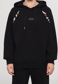 Černá mikina s kapucí s logem značky vpředu, s kontrastními pruhovanými látkovými detaily na ramenou a měkkým, strukturovaným povrchem.