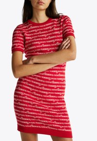 Rotes, figurbetontes Kleid mit kurzen Ärmeln, das ein wiederholendes weißes "Tommy Jeans"-Logomuster zeigt. Strukturiertes Gewebe mit geripptem Saum.