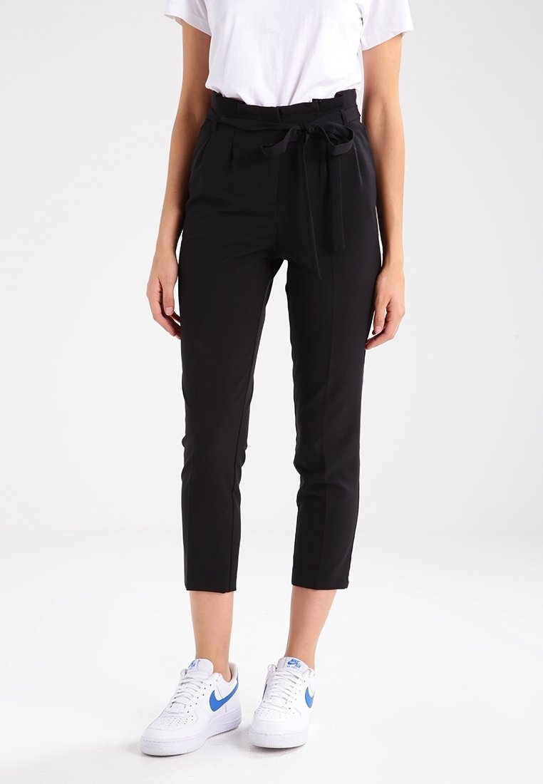 Svarta cropped byxor med hög midja, tygbälte och sidofickor, parat med en vit t-shirt och vita sneakers med blå detaljer.