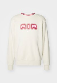 Sudadera crema con un destacado gráfico rojo y rosa de "AIR" en el frente y un pequeño logo blanco de Nike, con puños y cuello acanalados.