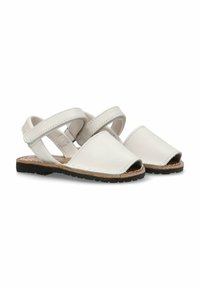 Las sandalias de cuero blanco presentan punteras abiertas, correas cruzadas, una suela plana y costuras decorativas. La suela está hecha de goma negra texturizada.