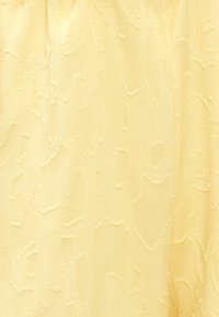 Tissu jaune texturé avec un motif en relief subtil, finition lisse et drapé fluide, adapté aux vêtements ou à l'ameublement.