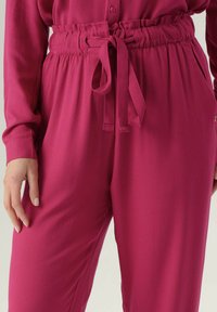 Pantaloni in tessuto rosa con taglio dritto, dotati di vita elastica e cordino da annodare, oltre a tasche laterali e una texture liscia.