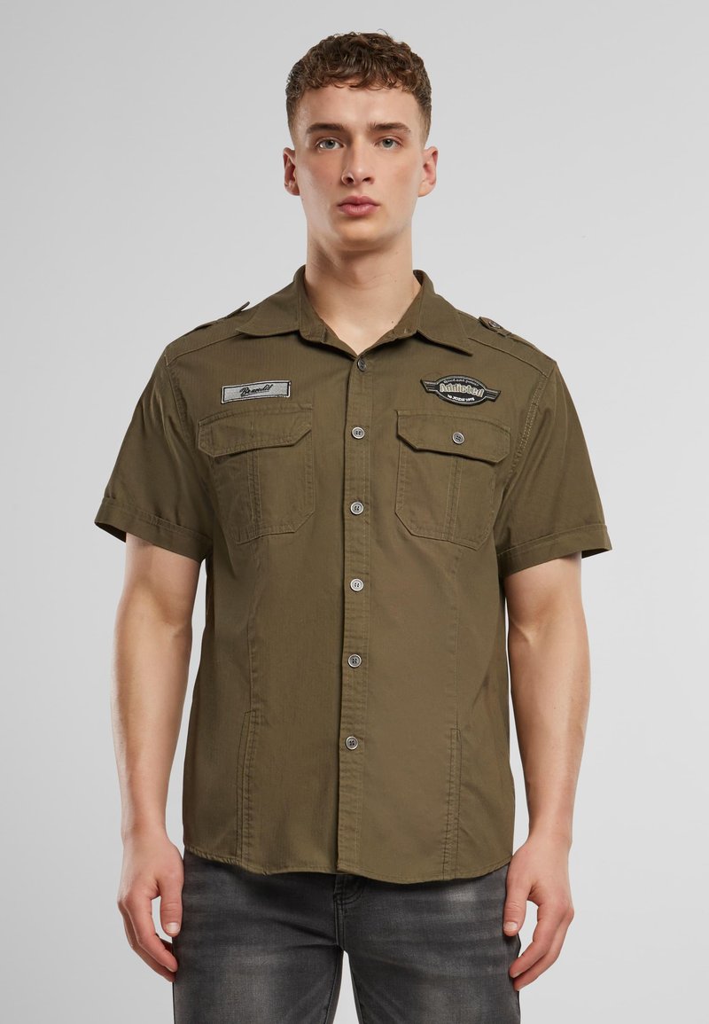 Kortermet olivengrønn skjorte med to brystlommer, knappelukking foran, skulderklaffer og broderte merkeaksenter.