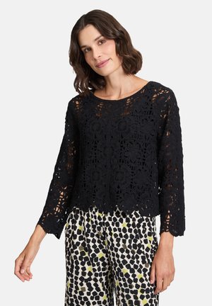 Top en crochet noir à dentelle avec des manches longues, des motifs floraux et un ourlet en forme de scallop, associé à un pantalon à pois et de couleur accent.