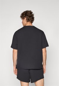 T-shirt en coton noir avec une coupe décontractée, des manches courtes et un col rond, associé à un short noir. La texture semble douce et décontractée.