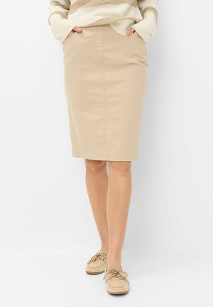 Personne portant une jupe beige longueur genou, mains dans les poches, associée à des chaussures beiges à lacets et un pull rayé crème et camel.