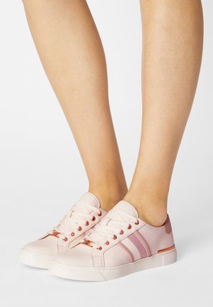 Vaaleanpunaiset tennarit sileällä viimeistelyllä, joissa on vaaleanpunaiset raidat, ruusukultaiset nyöri-reiät ja teksturoitu kangaspäällinen. Valkoinen kumipohja.