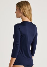 Marineblauw, lange mouwen top gemaakt van glad materiaal. Heeft een ronde halslijn en een getailleerd ontwerp, wat zorgt voor een strakke, minimalistische stijl.