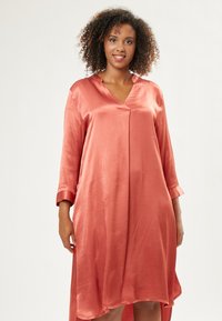 Vestido de satén en color coral con escote en V, mangas tres cuartos y un dobladillo asimétrico, con una textura suave y lisa.