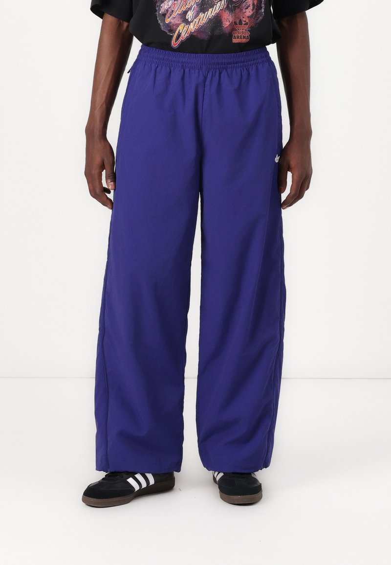 Pantalones de pierna ancha morados con cintura elástica, hechos de un material ligero, con bolsillos laterales y un acento de logo en el lado izquierdo.