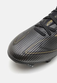 Black football boot featuring a textured surface with vertical stripes and gold accents. The design includes synthetic materials and a low-profile silhouette.