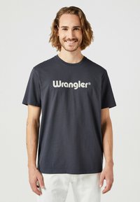 Mörk marinblå bomull T-shirt med en framträdande vit "Wrangler"-logotyp över bröstet, korta ärmar och rundad halsringning.