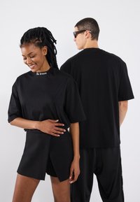 Sort bomulds oversized t-shirt med korte ærmer og "No drama" tekst ved kraven, parret med sorte shorts med en indpakningsdesign.