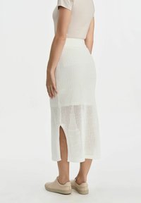 Biała, dzianinowa spódnica midi z teksturowanym wzorem, bocznym rozcięciem i elastycznym pasem, w połączeniu z beżowymi sneakersami i dopasowaną bluzką.