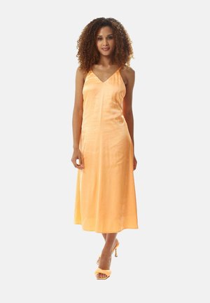 Satin orange midi dress with a V-neckline and thin straps. Smooth texture with a flowing silhouette. Paired with matching heeled sandals.