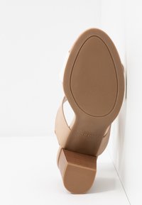 Sandale avec semelle en caoutchouc beige et talon bloc, montrant une adhérence texturée sur la semelle et le talon, sur fond blanc.