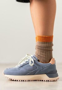 Zapatilla de lona azul con cordones blancos, suela rosa y un calcetín de rayas marrón y naranja, que presenta una tela texturada y un diseño elegante.