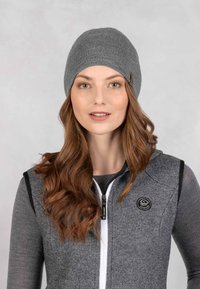 Szary dzianinowy beanie o gładkiej teksturze z logo z boku, w komplecie z szarym kamizelką z zamkiem błyskawicznym, mającą teksturowany design i czarne wykończenia.