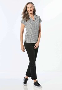 Kurze ärmelige Hemden mit Kragen im schwarz-weißen Muster, kombiniert mit schwarzen Hosen und schwarzen Sneakers. Geschmeidiger Stoff mit leichtem Glanz.