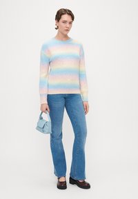 Παστέλ ριγέ πουλόβερ σε μπλε, ροζ και κίτρινο, συνδυασμένο με ανοιχτό μπλε τσάντα, φαρδιά τζιν και σκούρες καφέ πλατφόρμες.