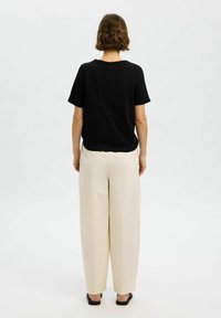 Svart bomullströja med korta ärmar, kombinerad med krämfärgade, vida byxor. Outfiten har en minimalistisk design och avslappnad passform.