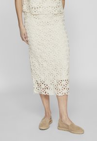 Hvit mønstrete heklede midiskjørt med blomsterdesign og bølget kant. Kombinert med brune espadrillos til en uformell stil.