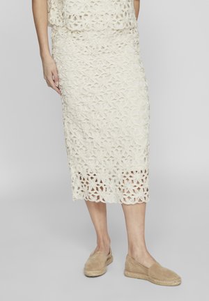 Hvit mønstrete heklede midiskjørt med blomsterdesign og bølget kant. Kombinert med brune espadrillos til en uformell stil.