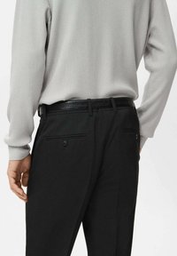 Mężczyzna ubrany w jasnoszary prążkowany sweter włożony w czarne spodnie wizytowe z czarnym teksturowanym paskiem, widok od tyłu od talii w dół.