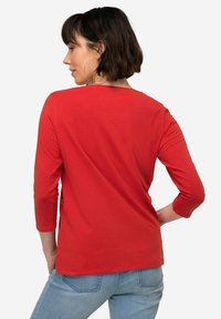 T-shirt rossa in cotone con maniche a tre quarti, scollatura rotonda e texture liscia. Abbinato a jeans azzurri chiari.