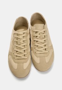 Baskets beiges à lacets en suède et textile, avec une texture lisse, un bout arrondi et des accents de design subtils.