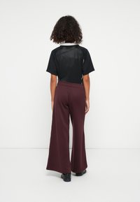 Juodas tinklinis trumpomis rankovėmis marškinėliai su apvaliu kaklu, derinami su bordo spalvos plačiomis kelnėmis. Abu drabužiai pasižymi laisvu siluetu ir elastingu juosmeniu.